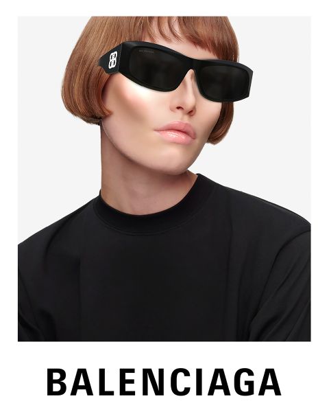 Eine Person mit futuristischer schwarzer Sonnenbrille und schwarzem Oberteil posiert vor hellem Hintergrund. Sie trägt einen kurzen, hellbraunen Bob. Unten ist deutlich das Balenciaga-Logo zu sehen.