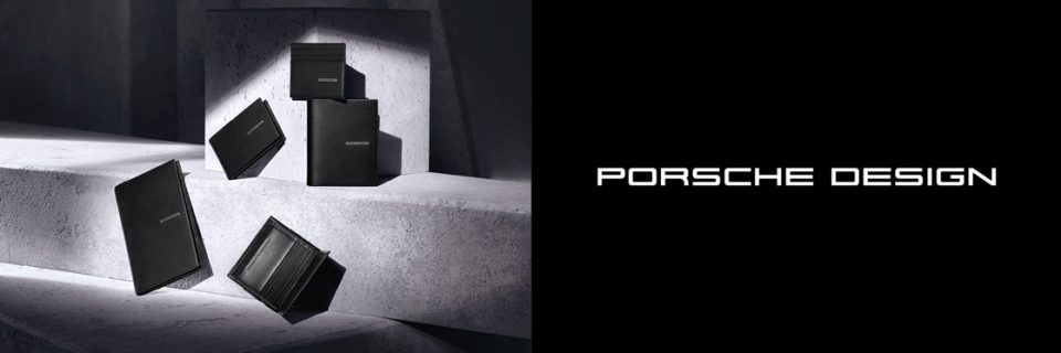 Eine Kollektion schwarzer Lederaccessoires von Porsche Design, darunter Geldbörsen und Kartenetuis, wird elegant auf Betonoberflächen präsentiert und wirft weiche Schatten. Das Porsche Design-Logo ist auf der rechten Seite prominent zu sehen.
