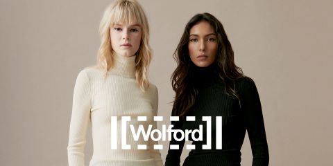 Zwei Frauen stehen nebeneinander und tragen figurbetonte Rollkragenpullover – eine in Creme, die andere in Schwarz. Sie stehen vor einem einfarbigen Hintergrund, auf dem das Wort „Wolford“ deutlich sichtbar quer über das Bild prangt.