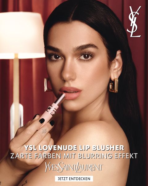 Eine Frau, die einen rosa YSL-Lip-Blusher nahe an ihre Lippen hält, mit einem deutschen Werbetext für den YSL Lovenuede Lip Blusher.