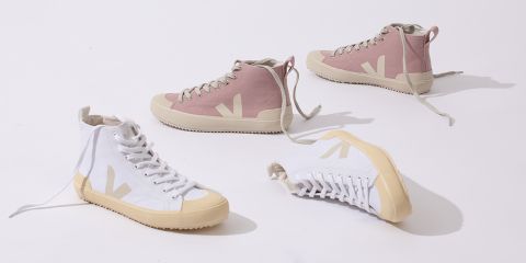 Ein Foto von vier High-Top-Sneakers mit sichtbaren Schnürsenkeln auf einer weißen Oberfläche. Zwei sind rosa mit beigen Sohlen und die anderen beiden sind weiß mit beigen Sohlen. Jeder Sneaker ist anders positioniert und zeigt verschiedene Winkel.