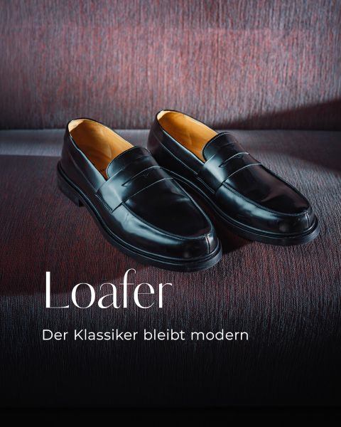 Ein Paar glänzende schwarze Loafer auf einer strukturierten dunkelroten Fläche, mit einem deutschen Schriftzug: „Loafer. Der Klassiker bleibt modern.“.