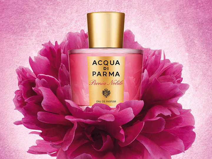 Eine rosa Flasche Acqua di Parma Peonia Nobile Eau de Parfum ist von leuchtend rosa Pfingstrosenblüten umgeben, die sich vor einem strukturierten rosa Hintergrund abheben. Der goldene Verschluss ergänzt das elegante und luxuriöse Design.