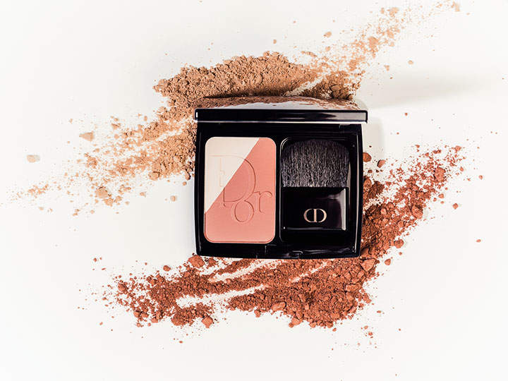 Kompakte Make-up-Palette mit Pfirsich- und Beigetönen, begleitet von einem kleinen Pinsel. Die Kompaktpalette ist geöffnet und pfirsichfarbener und brauner Puder ist auf einer weißen Oberfläche verstreut.