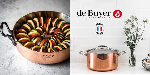 Ein Kupfertopf, gefüllt mit geschichteten Zucchini-, Auberginen- und Tomatenscheiben. Daneben steht ein Kupferkochtopf mit Deckel vor einer weiß gefliesten Wand mit Blumen in einer Vase. Das Logo von de Buyer und der Text „Made in France“ sind sichtbar.