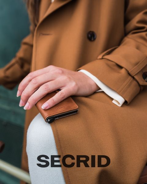 Eine Person im braunen Mantel hält eine kleine, braune SECRID-Geldbörse auf dem Knie. Am unteren Bildrand ist in großen Buchstaben das Wort „SECRID“ aufgedruckt.