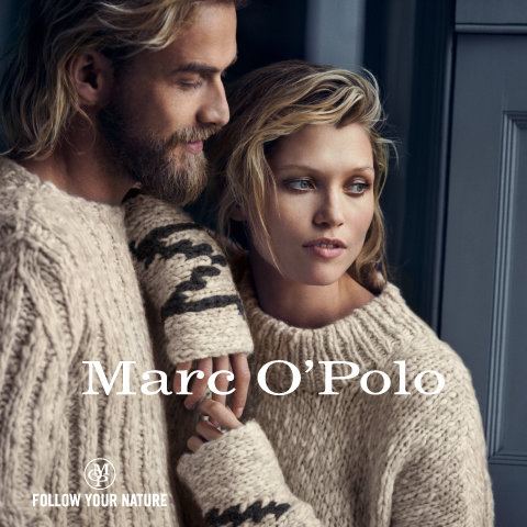 Ein Mann und eine Frau in kuscheligen Strickpullovern stehen dicht beieinander, darüber ist der Text „Marc O'Polo“ gelegt. Sie blicken zur Seite, mit einem ruhigen, nachdenklichen Gesichtsausdruck. Der Raum ist in sanften, gedämpften Farben gehalten.