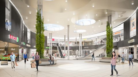 Ein geräumiges, modernes Einkaufszentrum mit hohen Decken und runden Oberlichtern. Die Käufer gehen und sitzen auf Bänken. Verschiedene Ladenschilder, wie zum Beispiel „SPAR“, sind sichtbar. Zwei zentrale Säulen sind von Grün umgeben, was einen Hauch von Natur verleiht.