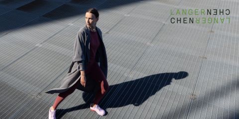 Eine Person in Sportkleidung und langem Mantel läuft auf einer Metallgitterfläche und wirft dabei einen Schatten. In der oberen rechten Ecke ist der grüne, abstrakte Text „LANGERNECHE“ zu sehen.