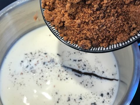 Brauner Zucker wird aus einer Schüssel in einen Topf mit Milch und Vanilleschoten gegeben.