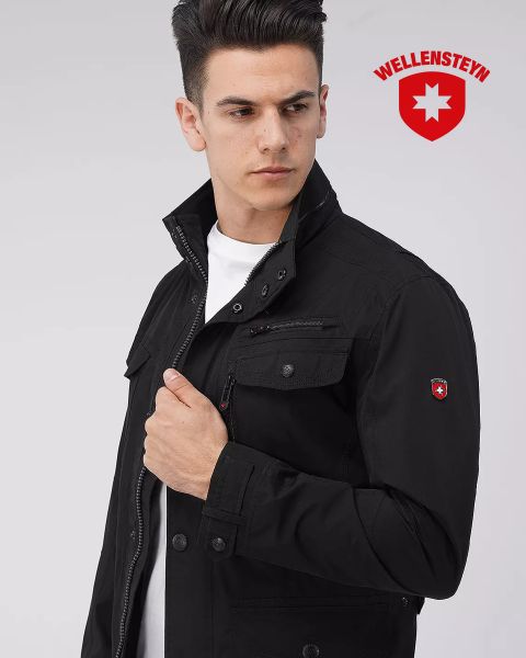 Eine Person in einer schwarzen Jacke blickt zur Seite. Die Jacke hat mehrere Taschen und einen Logo-Patch am Ärmel. Oben rechts ist das Wellensteyn-Logo abgebildet.