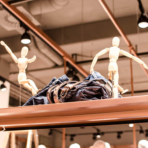Zwei hölzerne Schaufensterpuppen stehen in dynamischen Posen auf einem Regal und umgeben einen Stapel Jeanskleidung. Die Szene spielt in einem modernen Einzelhandelsgeschäft mit Beleuchtung und Dekor im Industriestil.