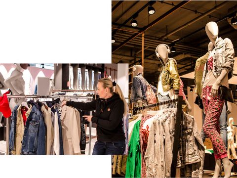 Eine Person stöbert in einem Geschäft nach Kleidung auf einem Ständer mit verschiedenen Stilen, darunter Jeans und Jacken. Mehrere Schaufensterpuppen präsentieren farbenfrohe Outfits auf einem anderen Ständer in einem gut beleuchteten Ladenlokal.