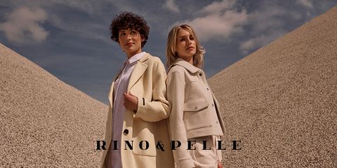Zwei Personen stehen im Freien vor einer Kulisse aus großen Kieshaufen und blauem Himmel. Sie tragen beigefarbene Kleidung. Am unteren Bildrand ist der Text „RINO & PELLE“ zu sehen.