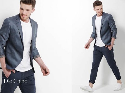 Ein Mann präsentiert ein lässiges Outfit bestehend aus einem blauen Blazer über einem weißen Hemd und einer schmal geschnittenen blauen Chinohose. Er trägt weiße Turnschuhe. Der Hintergrund ist schlicht weiß und links ist der Text „Die Chino“ zu sehen.