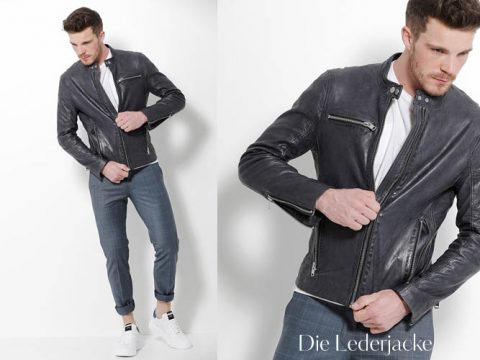 Ein Mann trägt eine schwarze Lederjacke über einem weißen Hemd und grau karierten Hosen mit weißen Turnschuhen. Er steht vor einem schlichten weißen Hintergrund und richtet die Jacke. Unten rechts ist der Text „Die Lederjacke“ zu sehen.