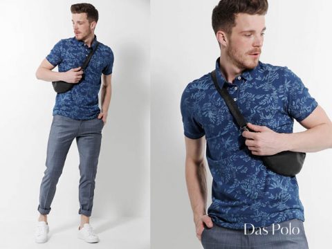 Ein Mann posiert in einem blauen Poloshirt mit Blumenmuster, grau karierten Hosen und weißen Turnschuhen. Er trägt eine schwarze Umhängetasche. Der Hintergrund ist schlicht weiß und in der unteren rechten Ecke ist der Text „Das Polo“ zu sehen.