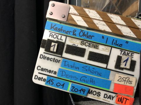 Eine Filmklappe mit der Aufschrift „Kastner & Ohler 'I Like'“ mit der Rollennummer 1, Szene 1 und Take 1. Als Regisseur ist Dustin Schöne, als Kameramann Denis Guth aufgeführt, als Datum ist der 15.01.2019 angegeben.