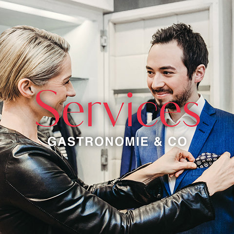 Eine Frau mit kurzen blonden Haaren rückt einem Mann im blauen Anzug das Einstecktuch zurecht. Sie lächeln sich in einem hell erleuchteten Raum an. Über das Bild sind die Worte „Services Gastronomie & Co“ gelegt.