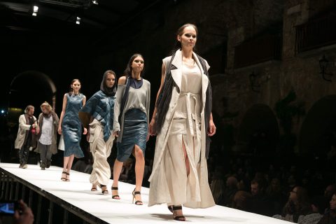 Bei einer Modenschau in einem eleganten Veranstaltungsort laufen Models in stylischen Lagen-Outfits vor den Augen des Publikums über den Laufsteg.