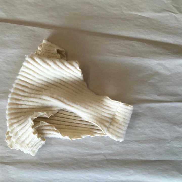 Ein gefalteter, cremefarbener Rippstoff liegt auf einer zerknitterten weißen Oberfläche. Die Textur und die Falten des Materials erzeugen Schatten und verstärken so sein weiches Aussehen.