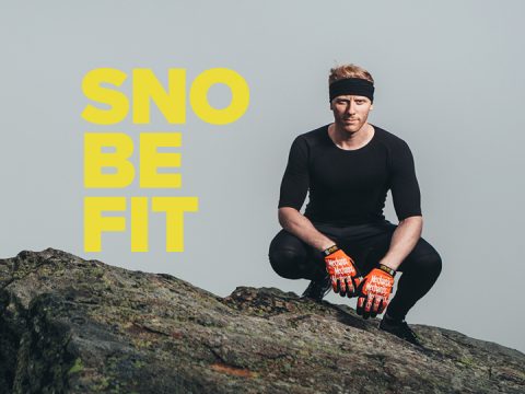 Eine Person in schwarzer Sportkleidung und orangefarbenen Handschuhen kauert auf einem felsigen Untergrund. Neben ihr steht in fetten gelben Buchstaben der Text „SNO BE FIT“.