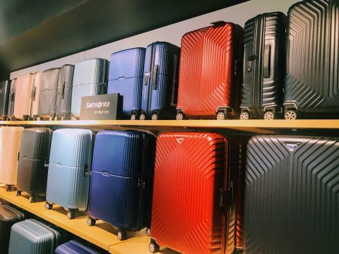 Auf Regalen sind verschiedene bunte Samsonite-Koffer ausgestellt. Die Gepäckstücke sind in verschiedenen Größen und Farben erhältlich, darunter Rot, Blau, Schwarz und Silber, und verfügen alle über einen stabilen Griff und Rollen.
