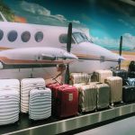 Eine Ausstellung verschiedener Koffer vor einem großen Wandgemälde mit einem weißen und braunen Flugzeug. Die Koffer sind in verschiedenen Farben und Mustern erhältlich, darunter Streifen und einfarbige, einige sind mit einem Sonderangebotsschild versehen.