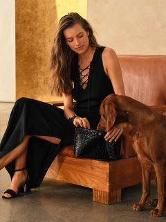 Eine Frau in einem schwarzen Kleid sitzt mit einem braunen Hund auf einem braunen Sofa und hält eine schwarze Handtasche auf ihrem Schoß.