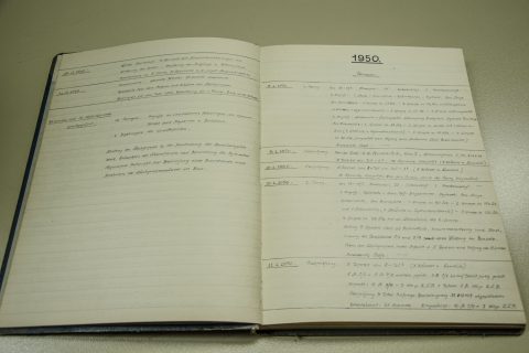 Ein offenes Buch mit handschriftlichen Einträgen aus dem Jahr 1950. Die Seiten enthalten Daten und Text, die vermutlich Ereignisse oder Aufzeichnungen dokumentieren. Die Einträge sind in einem sauberen, kursiven Stil auf liniertem Papier verfasst. Das Buch liegt auf einer flachen Oberfläche.