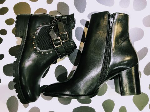 Zwei schwarze Stiefel auf einem gepunkteten Hintergrund. Der linke Stiefel ist mit Nieten und Schnallen versehen, während der rechte Stiefel ein elegantes Reißverschlussdesign und einen klobigen Absatz hat.