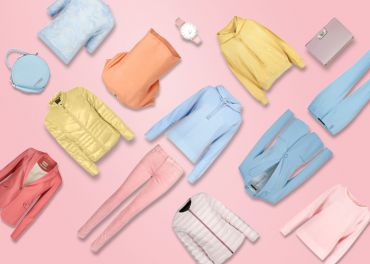 Eine flache Anordnung verschiedener pastellfarbener Kleidungsstücke und Accessoires vor einem rosa Hintergrund. Beinhaltet Jacken, Pullover, Hosen, eine Uhr, eine Geldbörse und eine Handtasche in den Farben Blau, Rosa, Gelb und Pfirsich.