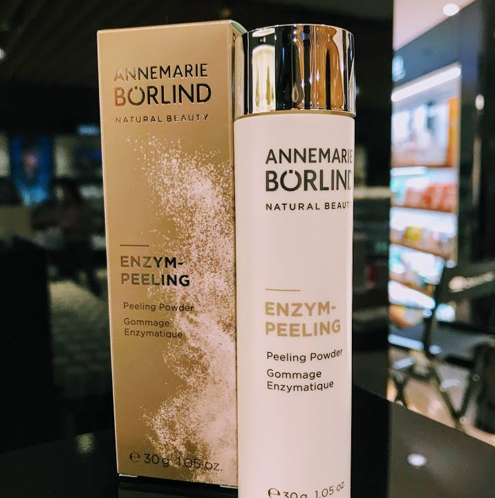 Eine Flasche Enzympeeling-Puder von Annemarie Börlind steht neben der Verpackung. Das Etikett weist darauf hin, dass es sich um ein natürliches Schönheitsprodukt handelt. Das Gewicht beträgt 30 g. Im Hintergrund ist ein schwach beleuchteter Innenraum zu sehen.