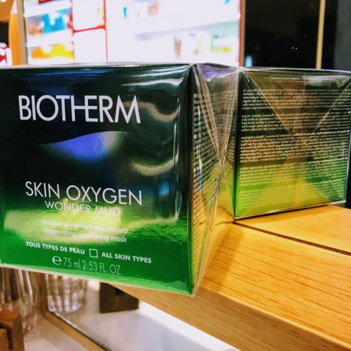 Eine Nahaufnahme von zwei Biotherm Skin Oxygen Wonder Mud-Boxen, die auf einem Regal ausgestellt sind. Die Verpackung ist grün mit weißem Text und zeigt, dass es sich bei dem Produkt um eine Sauerstoff spendende Reinigungsmaske für alle Hauttypen handelt.