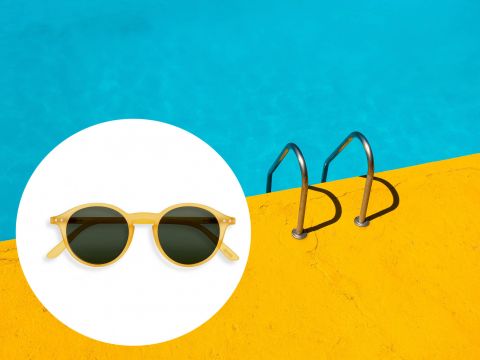 Links ist eine gelbe Sonnenbrille vor einem weißen, kreisförmigen Hintergrund zu sehen. Rechts führt ein leuchtend gelber Poolrand mit Metallgeländern in einen hellblauen Swimmingpool.