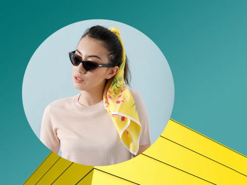 Eine Frau mit Cat-Eye-Sonnenbrille und einem gelben Schal im Haar vor einem blaugrünen Hintergrund. Sie befindet sich in einem runden Rahmen, der unten rechts ein geometrisches Design mit gelben Dreiecken überlagert.