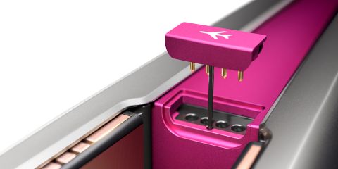 Nahaufnahme eines leuchtend rosa mechanischen Tastaturschalters, der in einen metallisch-silbernen Tastaturrahmen eingesetzt wird. Der Schalter verfügt über goldene elektrische Pins und ein kleines Logo mit einem nach unten gerichteten Pfeil.