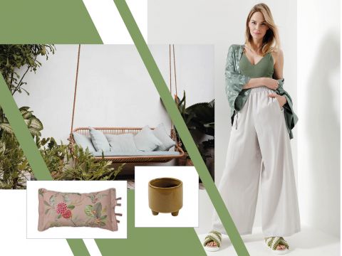 Eine Frau in einem grünen Oberteil und weißen Hosen steht selbstbewusst da. Grün akzentuiert den Hintergrund mit einer hängenden Gartenliege. Ein Blumenkissen und ein kleiner brauner Blumentopf vervollständigen die beruhigende, erdige Szene.