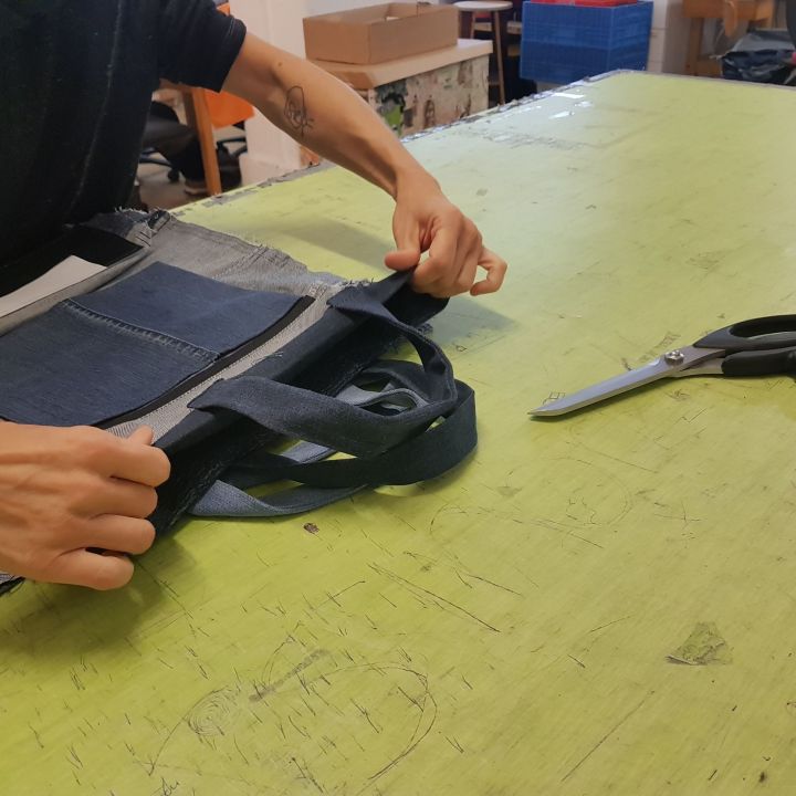 Person arbeitet an einem grünen Tisch mit einer Schere in der Nähe an einem Jeansstoffprojekt. Mit viel Liebe zum Detail entsteht ein Patchwork aus Jeansstücken.