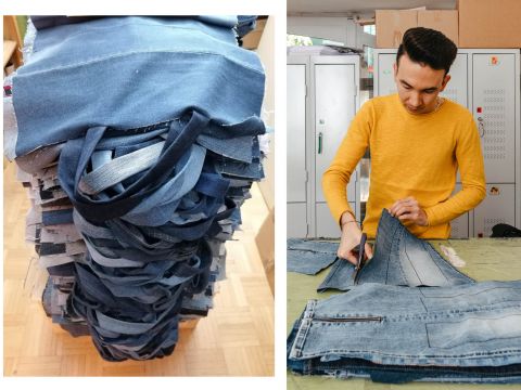 Eine Person in einem gelben Pullover schneidet Jeansstoff auf einem Tisch zu. Daneben liegt ein hoher Stapel gefalteter Jeansstoffstreifen mit Griffen, die wahrscheinlich zur Herstellung von Taschen oder anderen Gegenständen gedacht sind. Im Hintergrund sind Schließfächer und Kisten zu sehen.