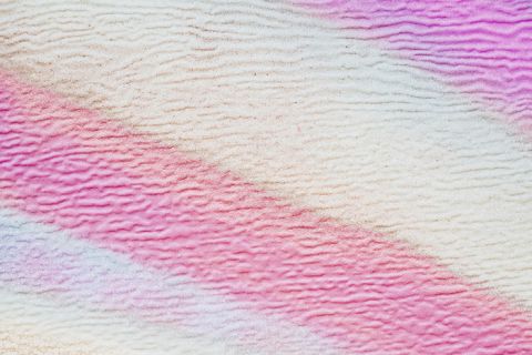 Abstraktes Bild mit weichen, gewellten Linien in Rosa-, Lila- und Weißtönen. Die Textur ähnelt einer gewellten Oberfläche und erzeugt ein beruhigendes, geschichtetes Muster.