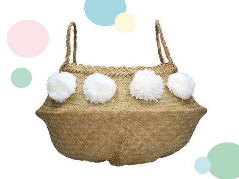 Ein geflochtener Korb mit Griffen ist mit fünf weißen Pompons verziert. Der Hintergrund besteht aus Kreisen in Pastellfarben: Rosa, Grün, Gelb und Blau.