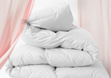 Ein Stapel weißer Kissen vor weißem Hintergrund, teilweise eingerahmt von durchsichtigen rosa Vorhängen an den Seiten. Die Kissen wirken plüschig und flauschig, lässig angeordnet.