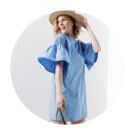 Eine Frau lächelt und trägt ein hellblaues Kleid mit ausgestellten Ärmeln. Sie trägt einen Strohhut auf dem Kopf und eine Handtasche. Der Hintergrund ist hell und schafft eine minimalistische und helle Atmosphäre.