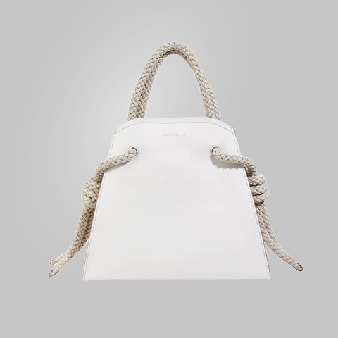 Eine weiße Handtasche im minimalistischen Design, mit geflochtenen Seilhenkeln und Knoten an den Seiten. Auf der Vorderseite ist der Markenname „Coccinelle“ eingeprägt. Der Hintergrund ist schlicht grau.