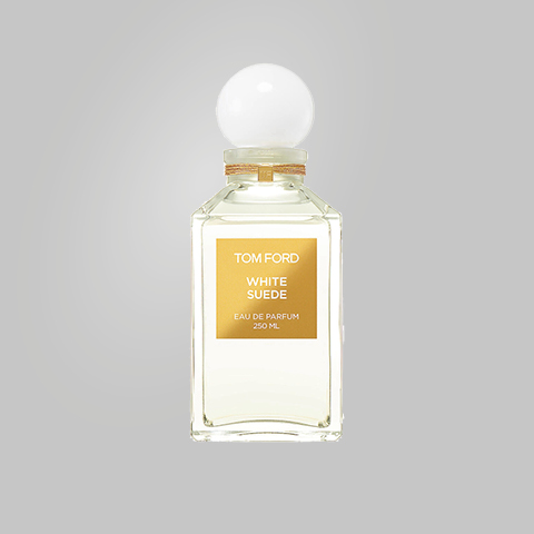 Eine Flasche Tom Ford White Suede Eau de Parfum ist vor einem schlichten grauen Hintergrund zu sehen. Die Flasche ist klar und rechteckig, mit einem weißen, runden Deckel und einem goldenen Etikett mit Produktdetails.