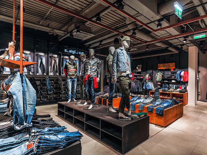 Ein trendiges Bekleidungsgeschäft mit Schaufensterpuppen in lässiger Kleidung, darunter Jeans und Jacken. Regale und Ständer zeigen eine Vielzahl von Jeansbekleidung unter heller Beleuchtung und schaffen so eine moderne und stilvolle Atmosphäre.
