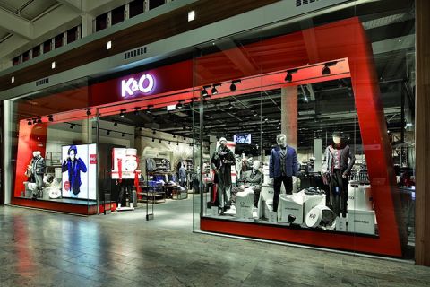 Schaufenster von K&Ö in einem Einkaufszentrum mit Schaufensterpuppen in verschiedenen Kleidungsstilen. Die Ausstellung umfasst Jacken, Hemden und Accessoires unter heller Beleuchtung, im Inneren sind weitere Kleidungsstücke zu sehen.