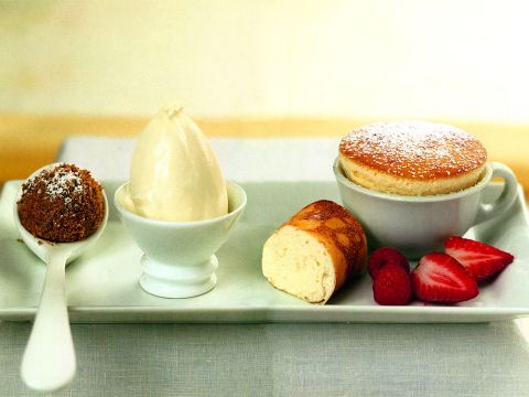 Ein Dessertteller mit einem Schokoladentrüffel auf einem Löffel, einer Kugel Vanilleeis in einer kleinen Schüssel, einer Portion Biskuitrolle und einem Soufflé in einer mit Puderzucker bestäubten Tasse, dazu Erdbeeren und Himbeeren.