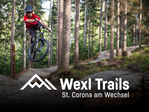 Mountainbiker im roten Trikot holt auf einem Waldweg bei Wexl Trails in St. Corona am Wechsel Luft. Hohe Bäume säumen den Feldweg. Im Vordergrund sind Logo und Ortstext zu sehen.